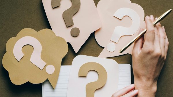 pexels-photo-5428833-5428833 Hands holding pen next to paper question marks on notebook, symbolizing inquiry and creativity.